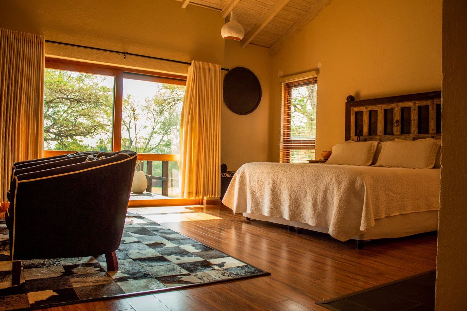 Spacious rustic bedroom inside a South African safari lodge with large glass doors looking out toward the trees.